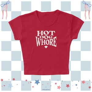 May include: A red crop top with the words "HOT DOG WHORE" in white, with a small heart below the text. The shirt has a round neckline and short sleeves. The background has a checkered pattern with stars and ribbons.