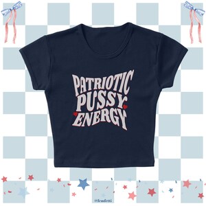 May include: Navy blue crop top with the text "PATRIOTIC PUSSY ENERGY" in white, with two small red hearts. The top has a scoop neck and short sleeves. The background has a patriotic theme with blue and white checkered squares and red, white, and blue accents.