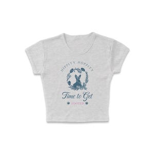 May include: A gray cropped t-shirt with a blue bunny rabbit graphic inside a wreath with the text "Hippity Hoppity Time to Get Zooted".