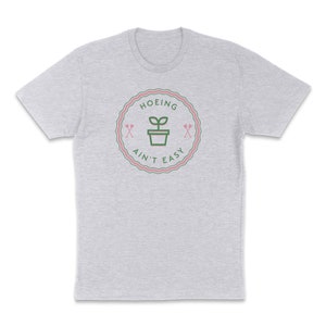 May include: A heather grey t-shirt with a green and pink graphic that says "Hoeing Ain't Easy" with a plant in a pot and two crossed gardening tools.