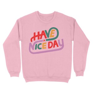 May include: Pink sweatshirt with the text "HAVE A NICE DAY" in a colourful, retro font.