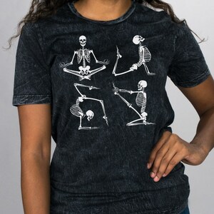 May include: Black t-shirt with a distressed look featuring white skeletons in various yoga poses.