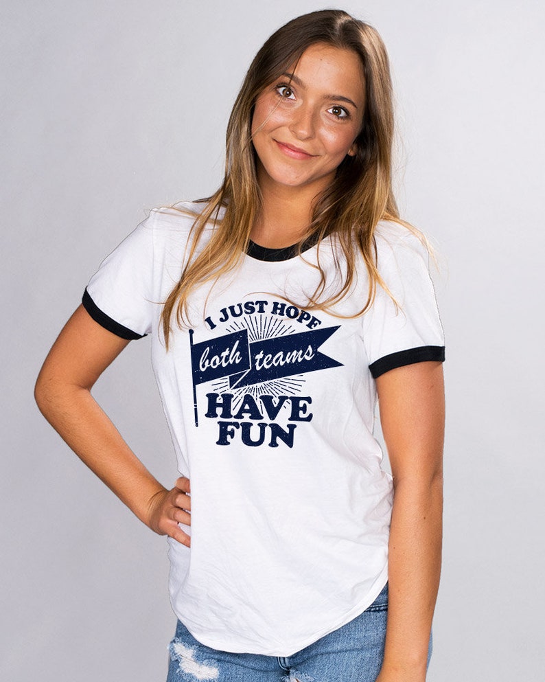 Puede incluir: Camiseta blanca con mangas negras de ribete, con un gr&aacute;fico azul que dice "I Just Hope Both Teams Have Fun" con un dise&ntilde;o de bandera vintage.