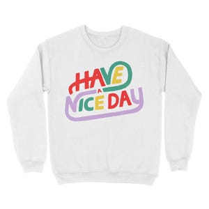 May include: White sweatshirt with a colourful graphic that says "HAVE A NICE DAY" in a retro style.