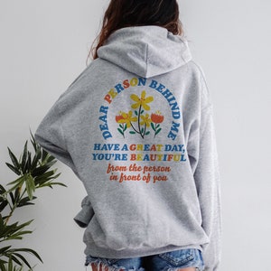 May include: Gray hooded sweatshirt with a colorful graphic on the back that says "Dear Person Behind Me Have a Great Day, You're Beautiful from the person in front of you".