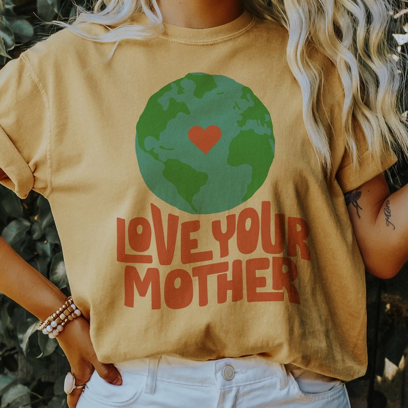 May include: A yellow t-shirt with a green and blue globe graphic and the text "LOVE YOUR MOTHER" in red and orange letters. The globe has a red heart in the center.