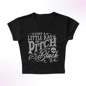 May include: Black cropped t-shirt with a white graphic that says "Just a little ray of pitch black" with a skull graphic.