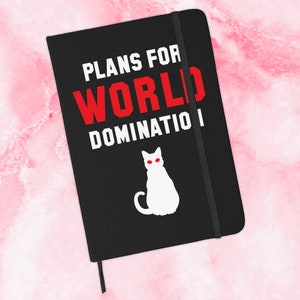 May include: Black notebook with a white cat illustration and the text "Plans for World Domination" in red and white.
