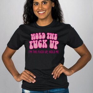 May include: Black t-shirt with pink text that reads "Hold the Fuck Up, I'm the Fuck Up, Hold Me."
