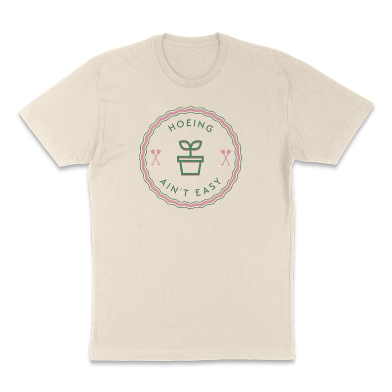 May include: A beige t-shirt featuring a green and pink graphic that reads "HOEING AIN'T EASY" with a plant in a pot and two crossed shovels.