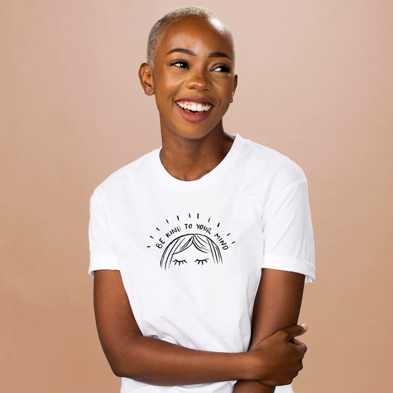 May include: White t-shirt with a black graphic design of a woman's face with the text "Be Kind to Your Mind".