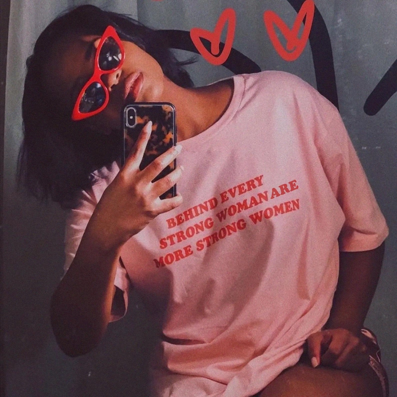 May include: A pink t-shirt with the text "Behind every strong woman are more strong women" printed in red.
