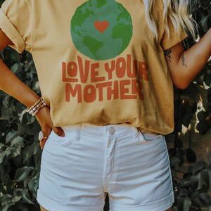 May include: A yellow t-shirt with a green and blue globe graphic and the text "LOVE YOUR MOTHER" in red and orange letters.