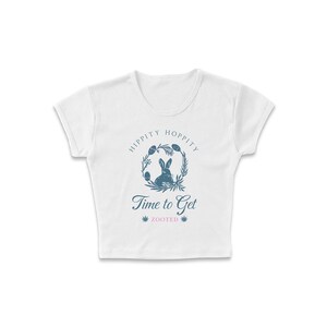 May include: White cropped t-shirt with a blue graphic of a rabbit in a wreath with the text "Hippity Hoppity Time to Get Zooted".