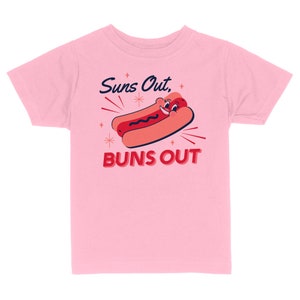 K&ouml;nnte beinhalten: Rosafarbenes T-Shirt f&uuml;r Kinder mit einem Cartoon-Hotdog mit einem l&auml;chelnden Gesicht und dem Text "Suns Out, Buns Out".