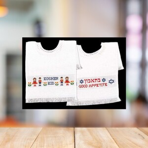 May include: Two white embroidered bibs with fringe trim. One bib says "Kosher Kid" with a boy and girl in the design. The other bib says "Good Appetite" in English and Hebrew.