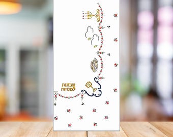 May include: A white greeting card with gold Hebrew text and decorative floral and symbolic elements. The design includes a menorah, birds, and a chalice, with red and gold accents. The card is set against a blurred background.
