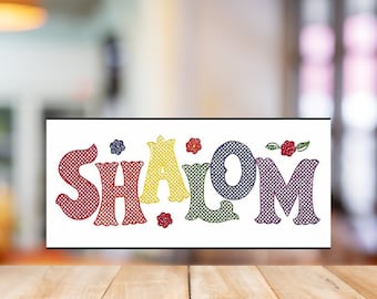 May include: A colorful sign with the word "SHALOM" in a rainbow pattern. The letters are outlined in black and have a checkered pattern. There are small flowers and leaves around the letters.