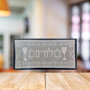 Pode incluir: Um corredor de mesa de crochê branco com as palavras hebraicas "L'chaim" e duas taças de vinho bordadas.