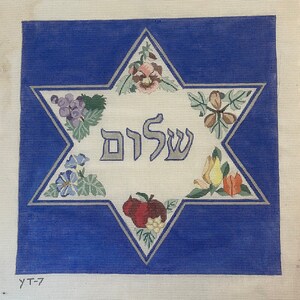 K&ouml;nnte beinhalten: Eine wei&szlig;e Leinwand mit blauem Hintergrund, auf der ein gro&szlig;er sechszackiger Stern mit dem hebr&auml;ischen Wort "Shalom" in der Mitte abgebildet ist. Der Stern ist von verschiedenen floralen und fruchtigen Motiven umgeben.