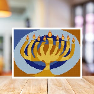 May include: A cross-stitch image of a gold menorah with nine lit candles. The menorah is set against a blue and gold background, with a white border. The image is displayed on a wooden surface.