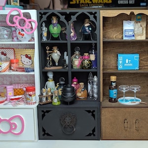 Puede incluir: Cuatro estantes de casa de muñecas en miniatura con diferentes temas. El primer estante es blanco con un lazo rosa y presenta artículos con el tema de Hello Kitty. El segundo estante es negro con una manija plateada y presenta botellas de pociones. El tercer estante es marrón con una manija de madera y presenta una bandeja pequeña con vasos. El cuarto estante es azul con bordes festoneados blancos y presenta suministros para hornear.
