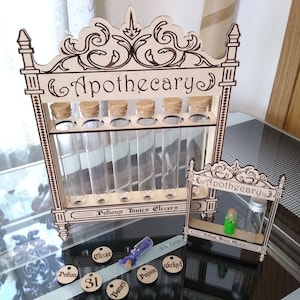 May include: Wooden apothecary stand with six glass test tubes and cork tops. The stand has a decorative scrollwork design and the words "Apothecary" and "Potions Tonics Elixirs" are engraved on the front. There is a smaller apothecary stand with a single test tube containing a green liquid.