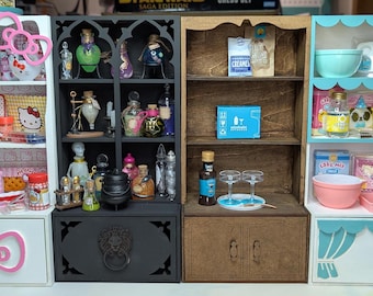 May include: Three white miniature dollhouse shelves with different themes. The left shelf is pink and white with a Hello Kitty theme. The middle shelf is black with a witchy potion theme. The right shelf is white with a blue and teal trim and a baking theme.