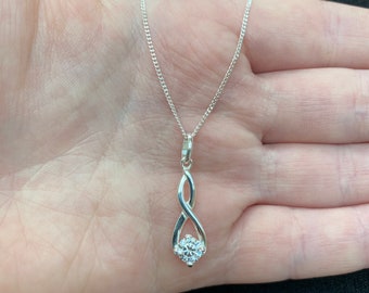 Puede incluir: Un collar de plata con un colgante retorcido con una piedra redonda transparente.