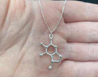 May include: A silver necklace with a pendant shaped like the molecular structure of caffeine.