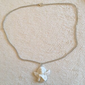 Op de afbeelding: Een zilveren ketting met een witte porseleinen engelhanger. De engel is afgebeeld met vleugels en gevouwen handen.