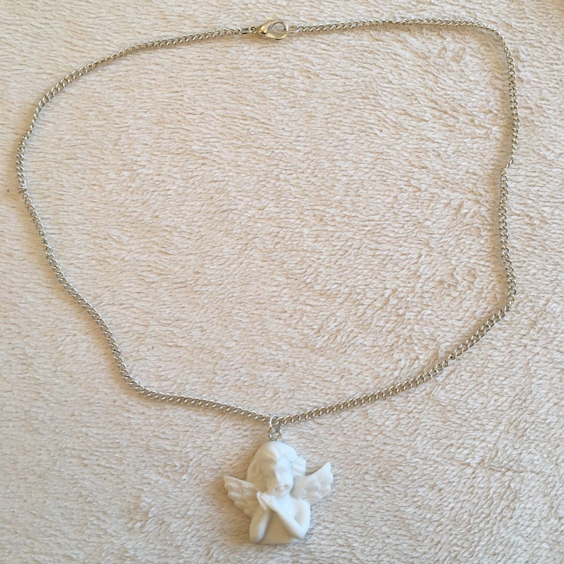 Op de afbeelding: Een zilveren ketting met een witte porseleinen engelhanger. De engel is afgebeeld met vleugels en gevouwen handen.