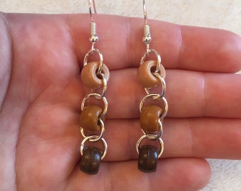 May include: A pair of dangle earrings with a silver chain and brown and beige wooden beads.