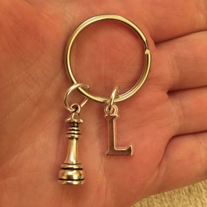 Op de afbeelding: Zilveren sleutelhanger met een schaakstuk-hanger en een letter L-hanger.