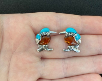 May include: A pair of silver earrings featuring a turquoise and amber bird design.