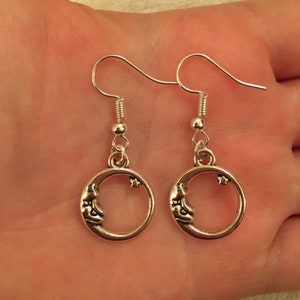 Pode incluir: Brincos de prata com forma de lua crescente e estrela. Os brincos têm um design simples com uma lua crescente e uma estrela.