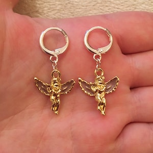 Puede incluir: Un par de pendientes de &aacute;ngel dorados con aros de plata. Los &aacute;ngeles tienen alas y sostienen un coraz&oacute;n.