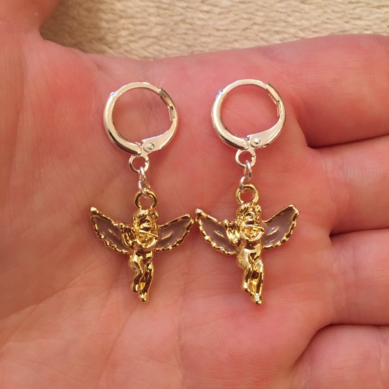 Puede incluir: Un par de pendientes de &aacute;ngel de oro con aros de plata. Los &aacute;ngeles tienen alas y sostienen un coraz&oacute;n.