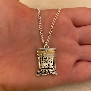 Może przedstawiać: Srebrny naszyjnik z łańcuszkiem i srebrnym zawieszką w kształcie torebki chipsów. Na torebce widnieje napis "Potato Chips".