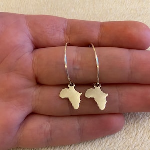 Könnte beinhalten: Ein Paar silberne Creolen mit einer silbernen Umrandung des afrikanischen Kontinents, die an jeder Creole hängt.