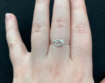 Op de afbeelding: Een zilveren knoop ring aan een vinger.