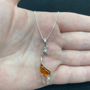 Op de afbeelding: Een zilveren giraffenhangerketting met een amberen steen inleg. De ketting is aan een zilveren ketting.