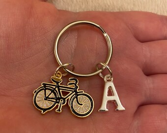 May include: A silver key chain with a black and gold bicycle charm and a silver letter A charm.