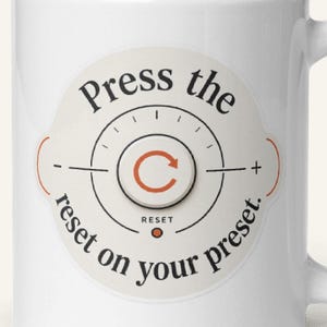 May include: A white ceramic mug featuring a circular graphic design with a central reset button icon. The text reads, Press the reset on your preset, arranged in a circle around the icon. The design includes a small orange arrow and dot.
