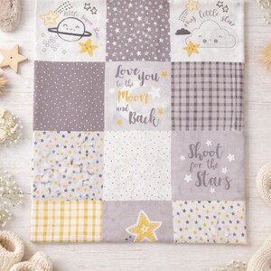 May include: A patchwork baby blanket with a celestial theme. The blanket features various gray, white, and yellow star patterns and phrases like "Love you to the Moon and Back" and "Shoot for the Stars". The blanket is approximately 24 inches square.