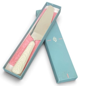 Può includere: Una paletta per dolci color argento con un manico color crema caratterizzato da un motivo a foglie in rilievo, riposta in una scatola azzurra foderata con tessuto rosa. Il coperchio azzurro riporta la scritta LENOX in bianco con accenti rosa.