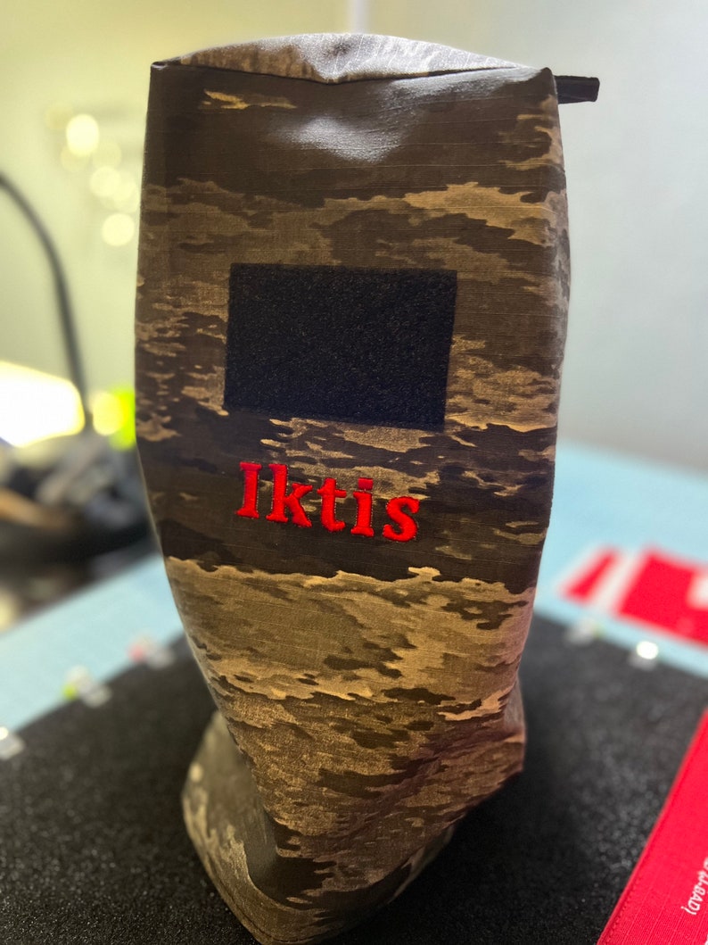 May include: A camouflage-patterned fabric pouch with a black velcro patch and the word "Iktis" embroidered in red.