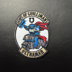 May include: Embroidered patch featuring a blue armored figure riding a motorcycle, wielding a hammer. The patch includes the text "SONS OF GUILLIMAN" and "ULTRAMAR" on a white and black background, with a red cape.