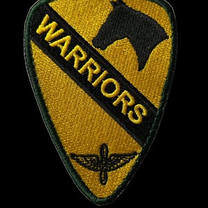 Puede incluir: Un parche bordado amarillo y negro con una cabeza de caballo y la palabra "WARRIORS" en letras negras. Un símbolo alado negro y amarillo se encuentra en la parte inferior del parche.