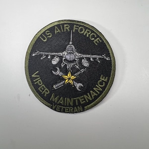 May include: A circular patch with the text "US AIR FORCE VIPER MAINTENANCE VETERAN". The patch features a fighter jet, wrenches, and a star in yellow and white against a black background.
